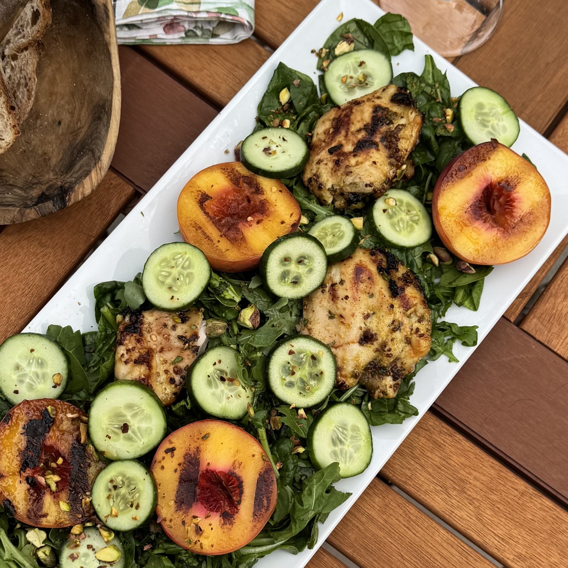 Grilled chicken and peach salad with cucumber, arugula, and pistachios on a white platter